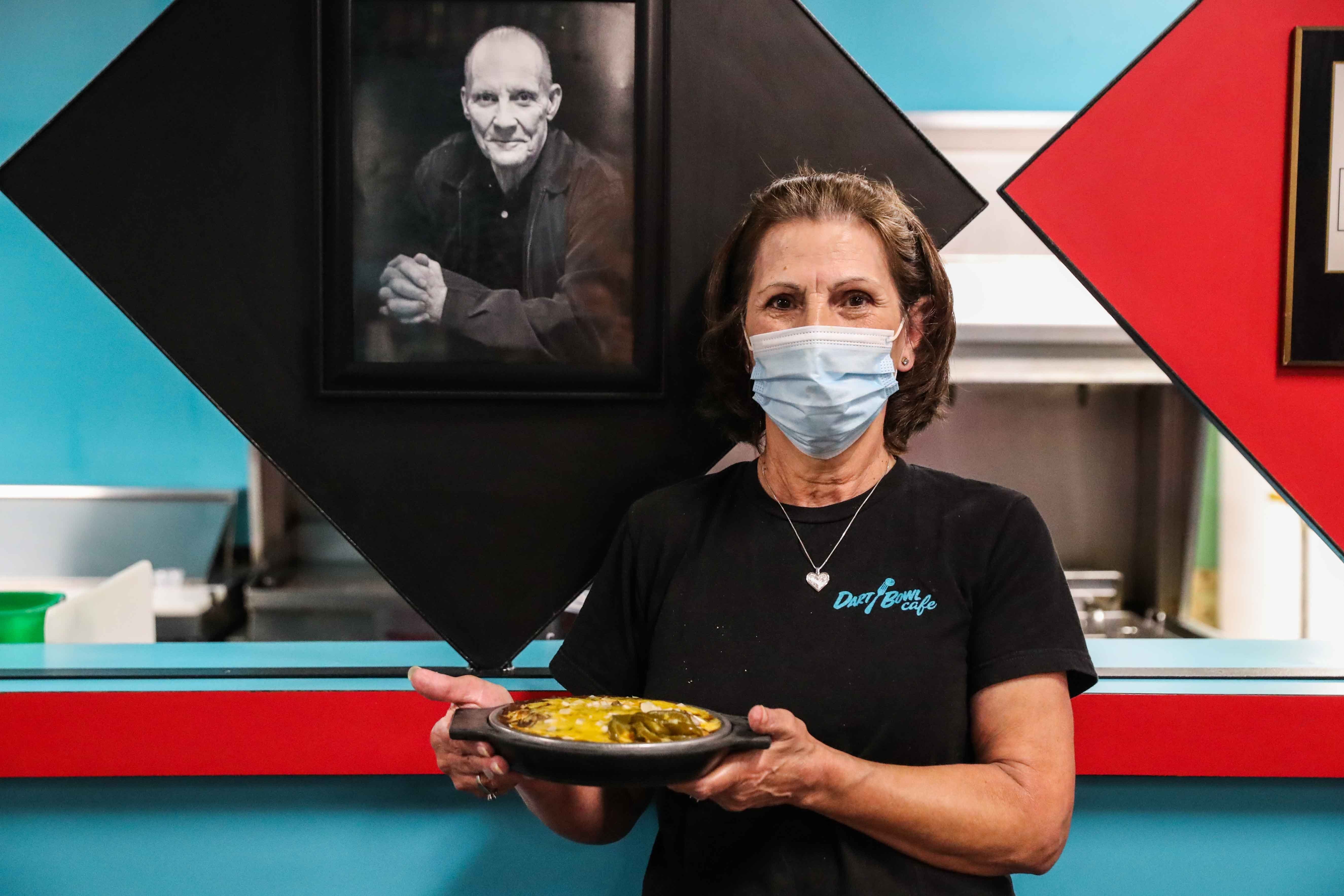 Peggy Zamarripa poses next to a photo of Dart Bowl Cafe founder Butch Martinets as she holds her famous enchiladas.
